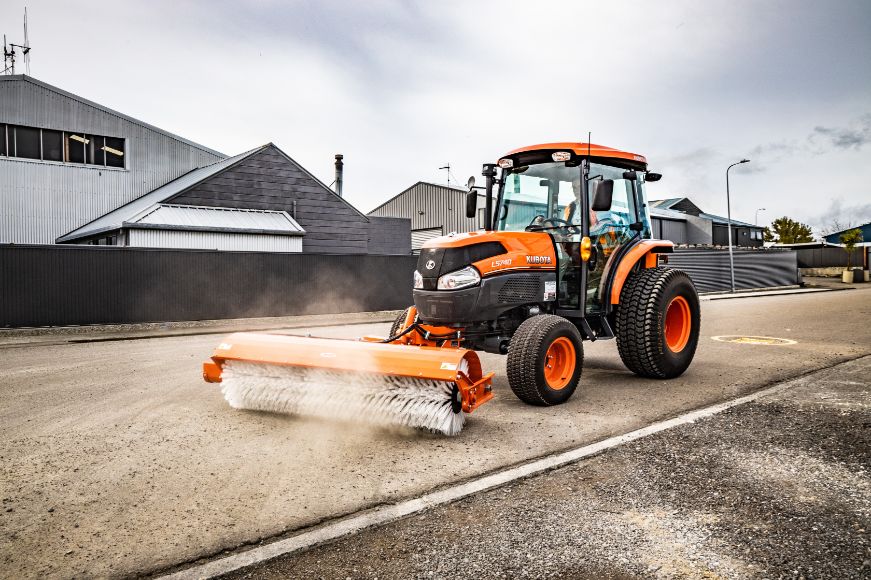 Side view of Orange Kubota Tractor sweeping a Street